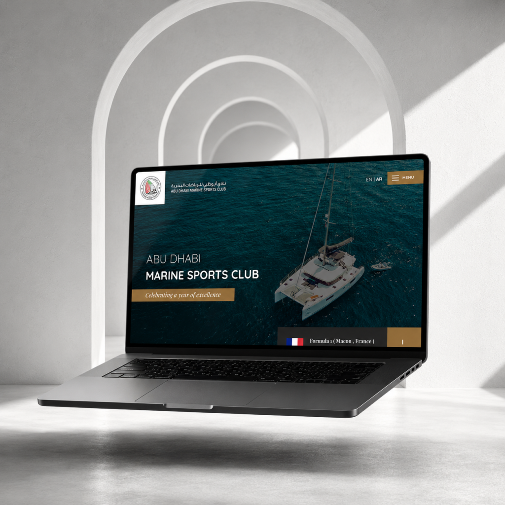 Abu Dhabi Marine Sports Club website on a laptop showing a yacht at sea with the line 'Celebrating a year of excellence', in English and Arabic.